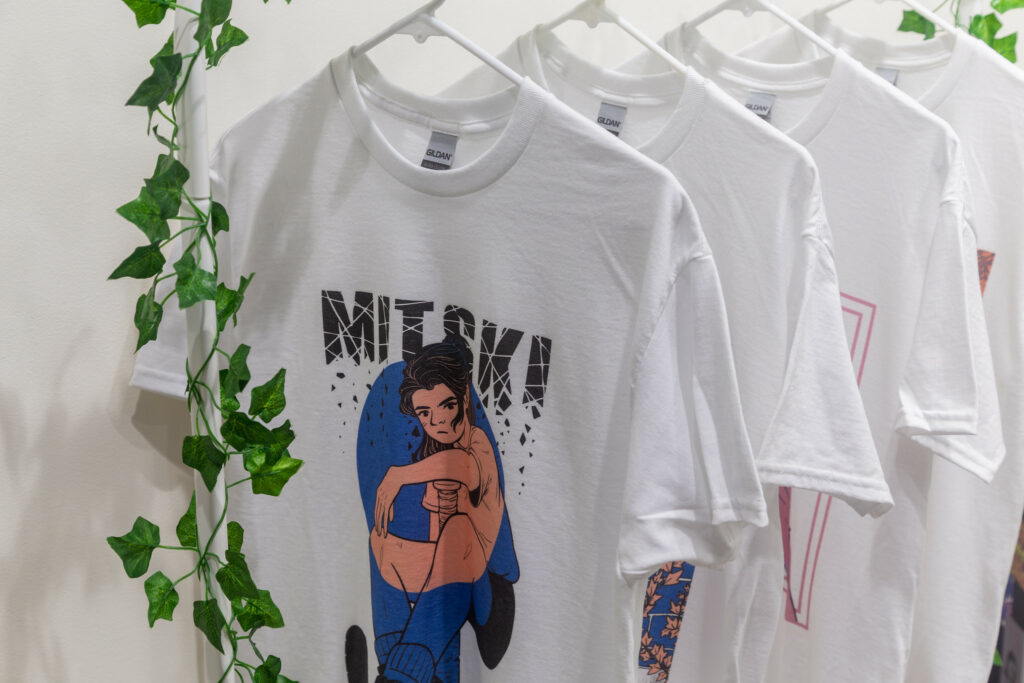 A shirt including an illustration of a young person and the crumbling words "Mitski" above it