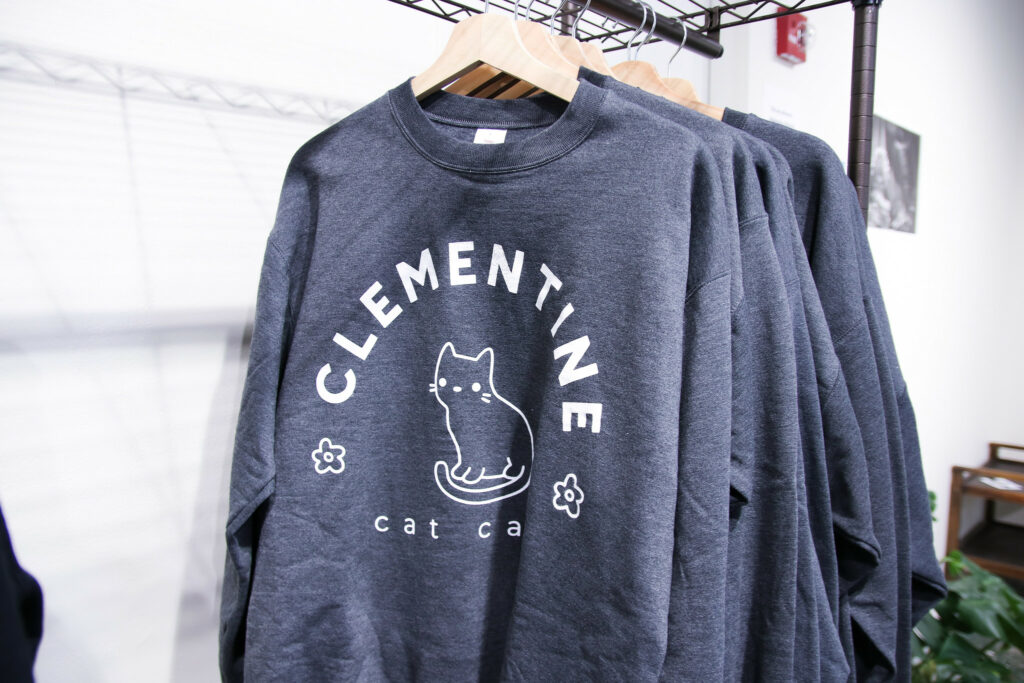 A series of sweaters with the words "CLEMENTINE cat cafe" written around a cutesy drawing of a cat