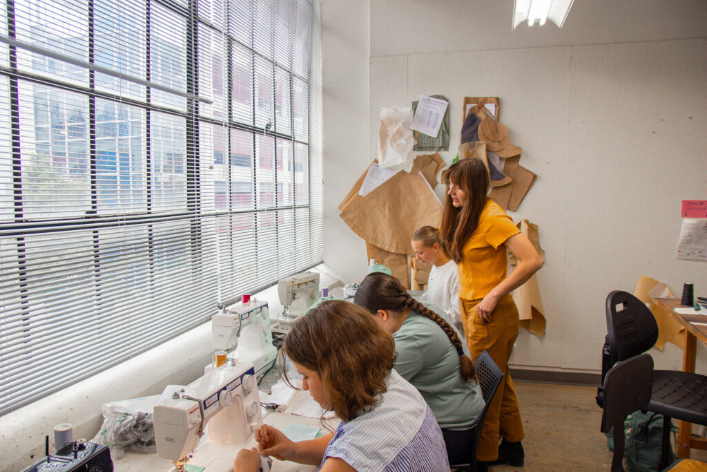 Instructor talks to three teens while they sew clothing.