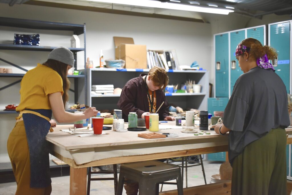 two students and an instructor work on ceramics at a table