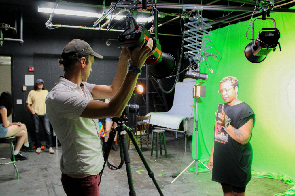 Instructor pointing lighting at subject in front of a green screen. Students are in the background.