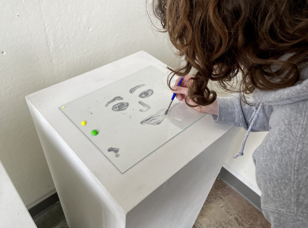 Someone practice paint-on-glass by painting a silver face on a piece of glass
